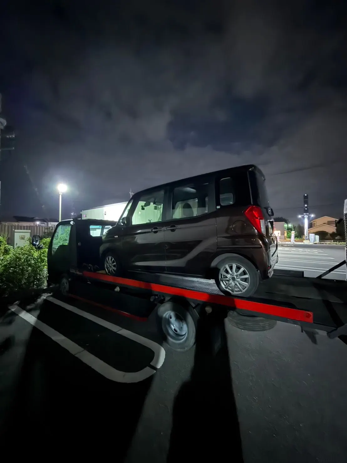 夜の駐車場で、積載車に軽自動車を載せている